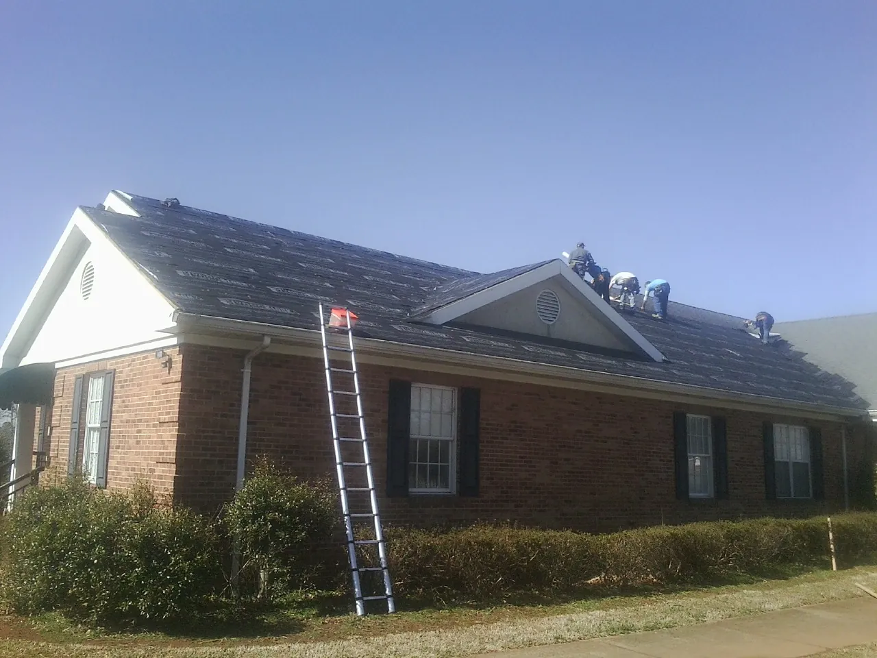 Crew tearing shingles off a brick ranch roof with a ladder set — Emergency Roof Repair work by our crew in Middlefield
