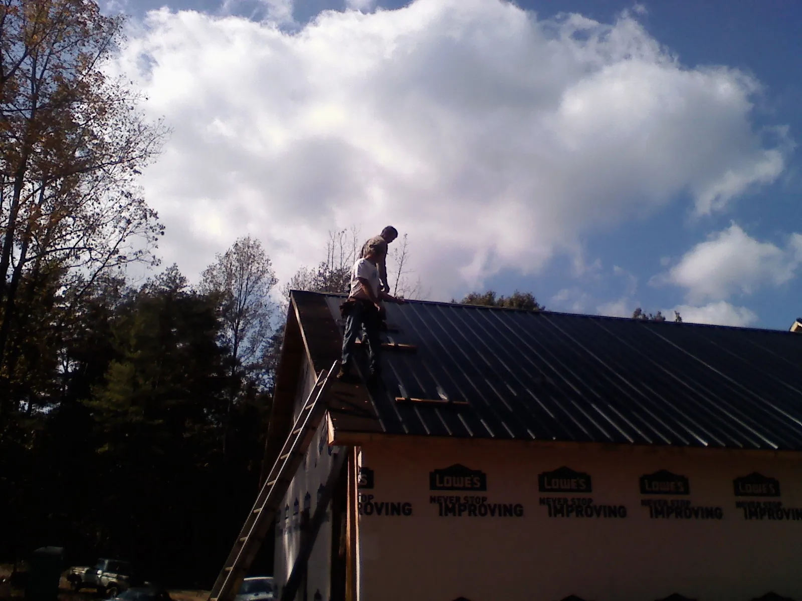 Roofer fastening dark metal panels high against a cloudy sky, from a Roof Inspection job in Middlefield
